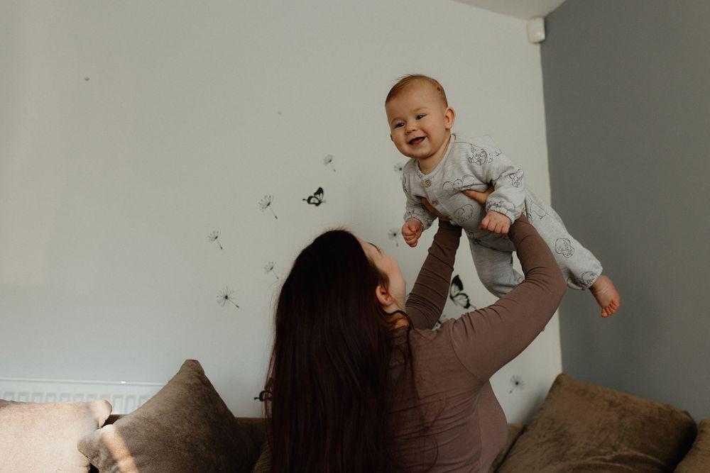 A joyful moment captured as a baby is lifted high in the air while playing on a couch at home.
