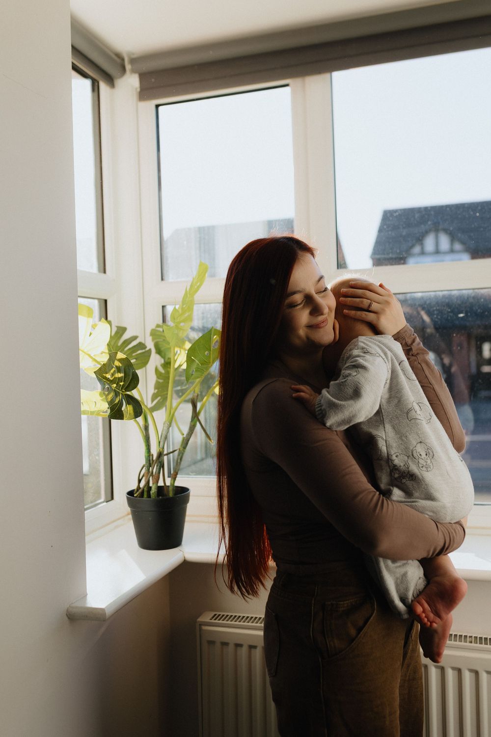 A series of photos showing a tender moment between a person and their pet cat by a bright window with houseplants.