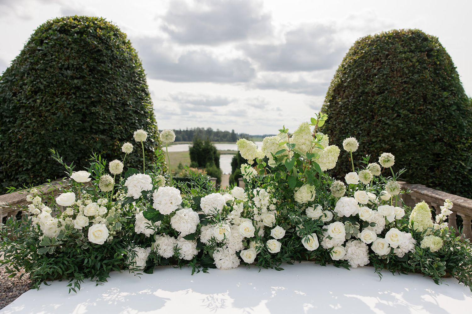 White roses and floral arrangements between two manicured topiary bushes in an elegant garden setting.