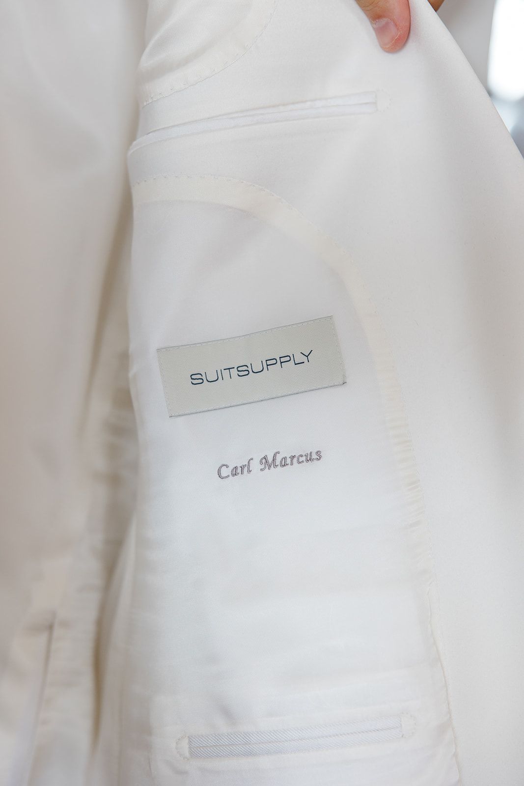 Close-up view of white suit jacket label showing Suit Supply and Carl Marcus branding details.