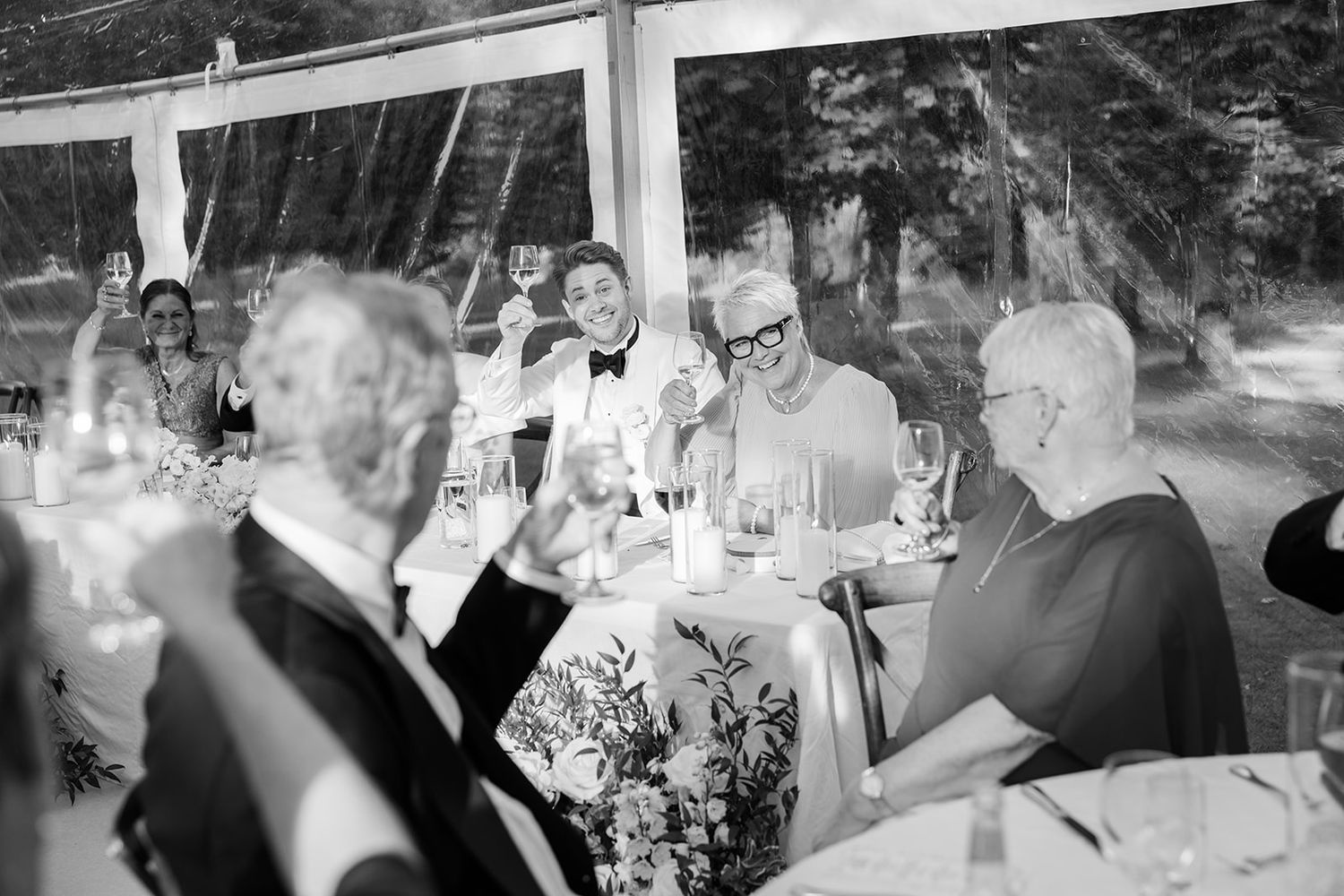 People gathered around a table enjoying drinks and conversation at an outdoor dinner party in black and white.