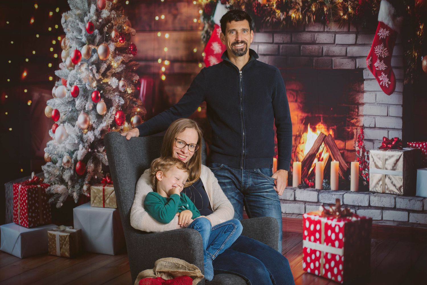 A festive Christmas photo session with a decorated tree and red brick wall backdrop in a cozy indoor setting.