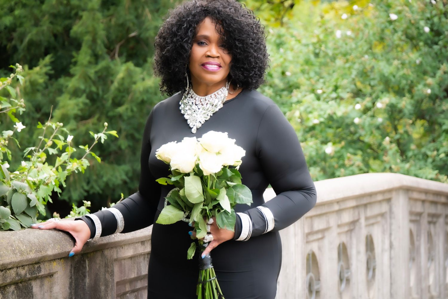 Professional outdoor photoshoot with black outfit and white flowers against stone architecture.