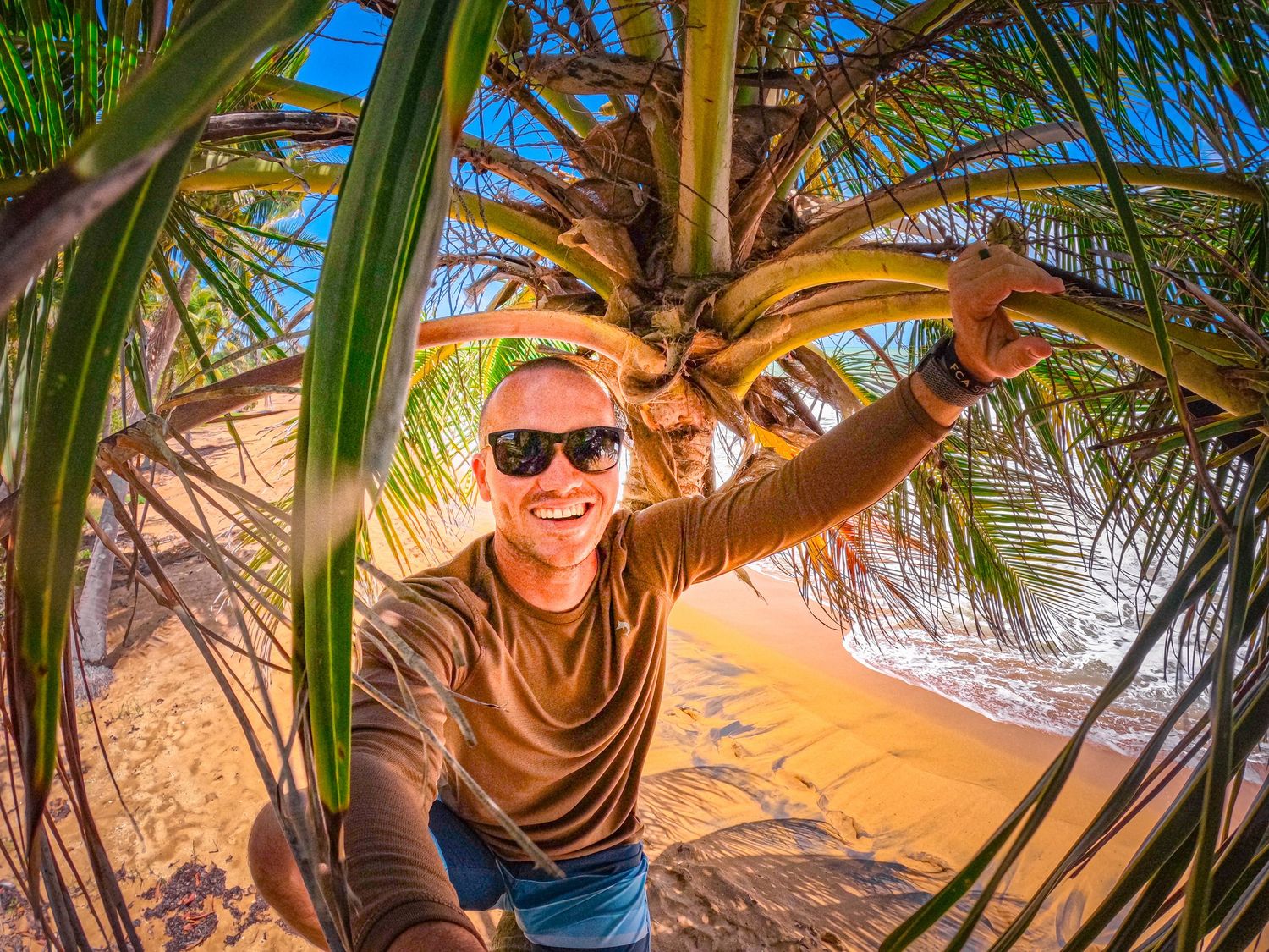 Memory Lain Photography owner, JJ, sitting in palm tree wearing sunglasses and smiling on a beach in Puerto Rico