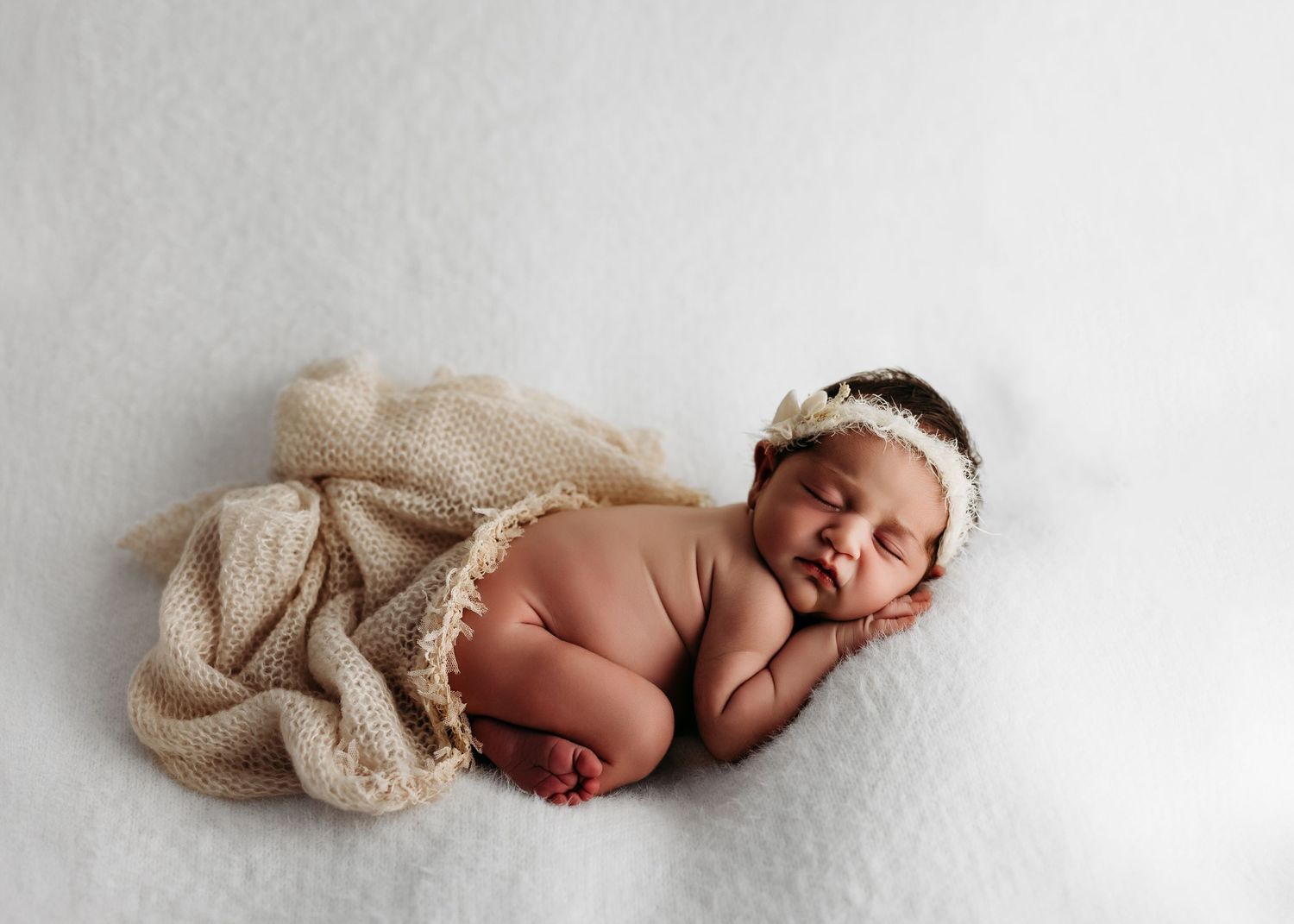 A sleeping newborn baby on white backdrop wearing lace headband and wrapped in beige knit blanket. Rashinphotography - Nova photographer DMV