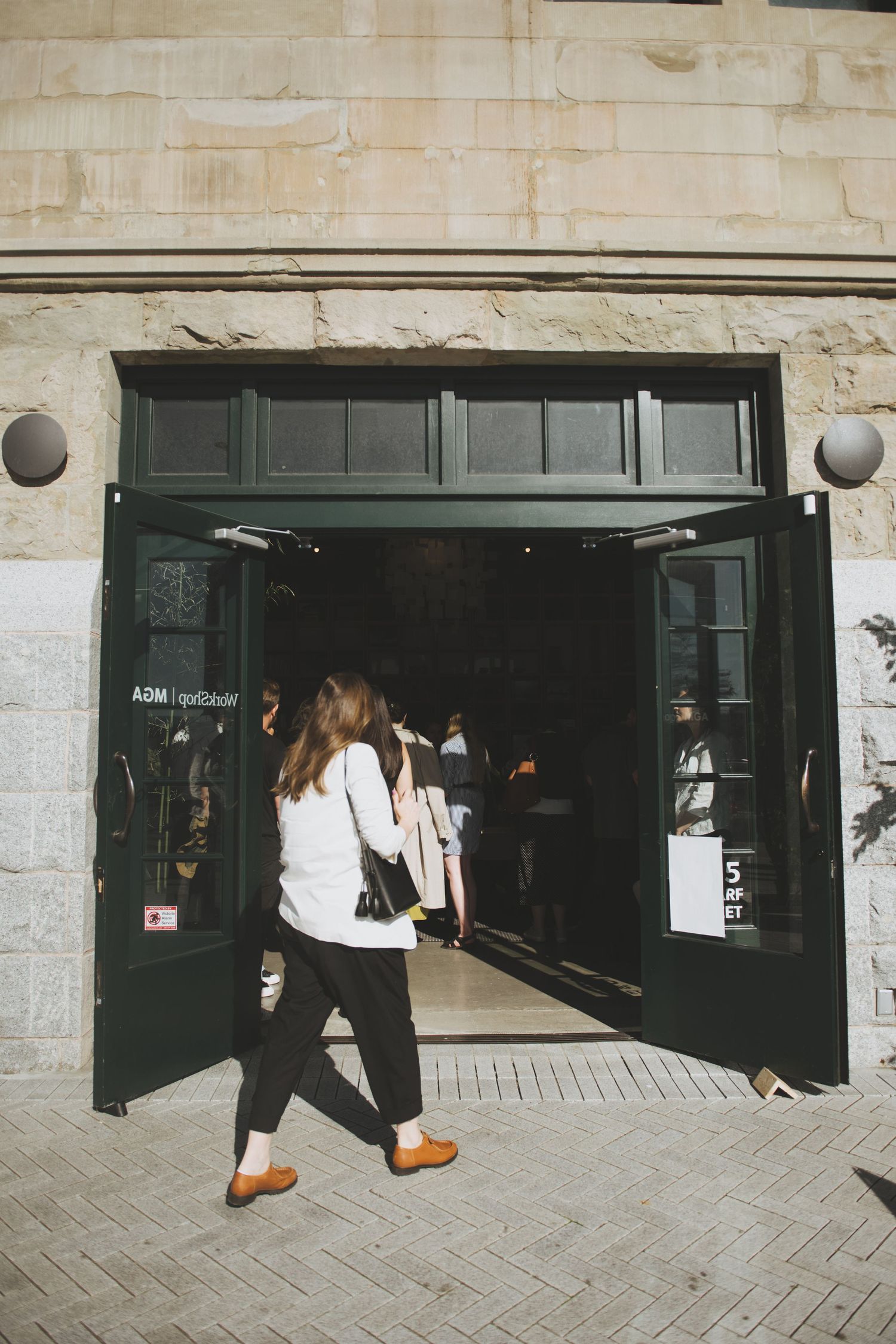 A woman entering a storefront event with a dark green doorway and white stone facade on a cobblestone street.