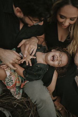Candid moment of parents tickling laughing child during outdoor photoshoot.