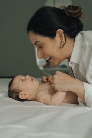 Sweet interaction between caregiver and baby on white bedding.