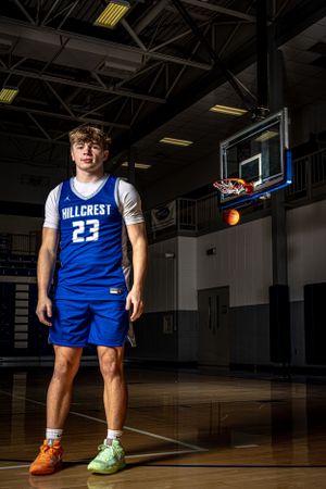 Basketball player stands on court with hoop and ball visible in dramatic indoor lighting.