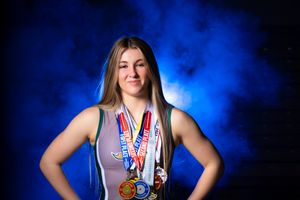 Athlete poses with multiple medals against dramatic blue smoke backdrop.