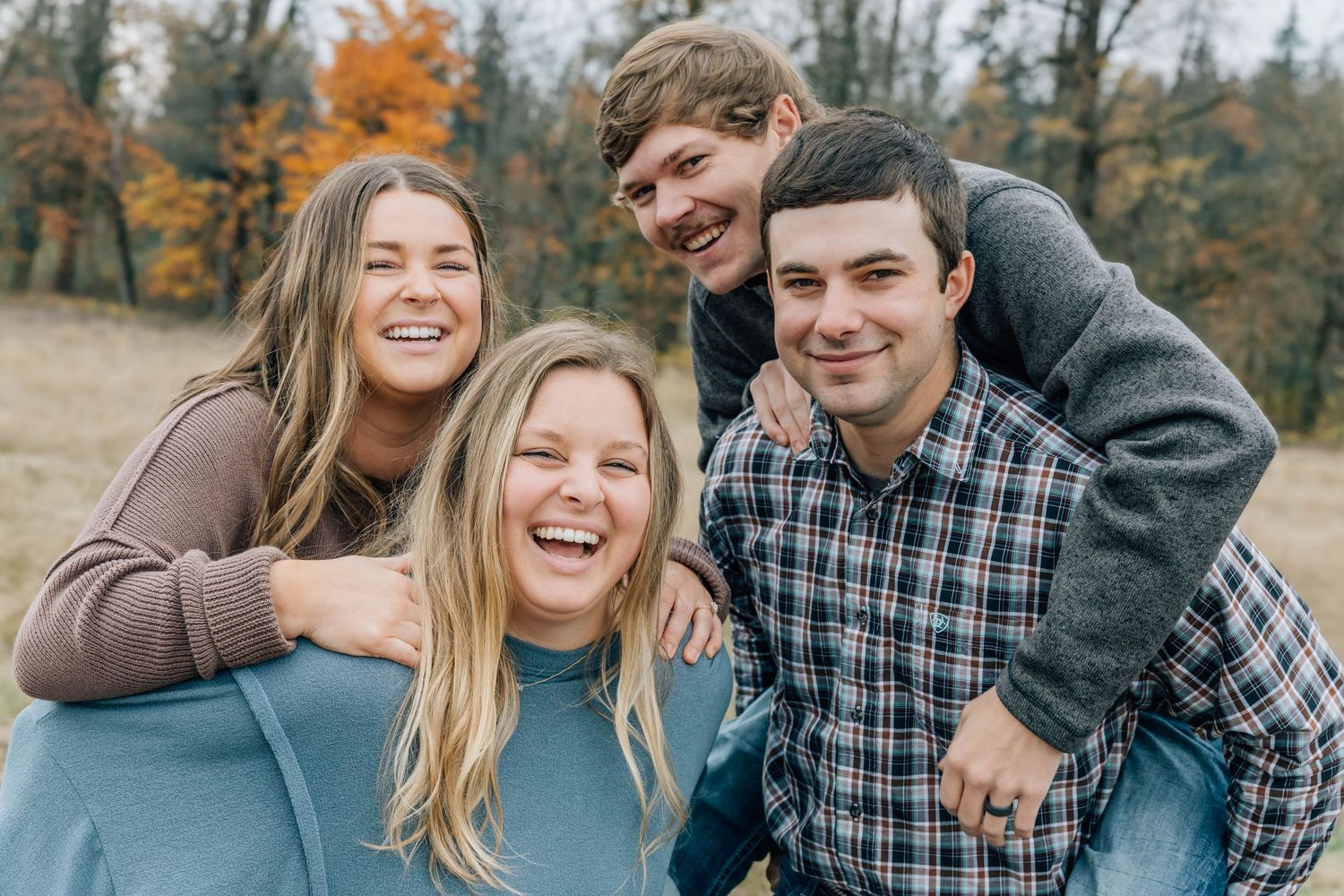 Four young adults laugh and hug together outdoors in a colorful autumn setting.