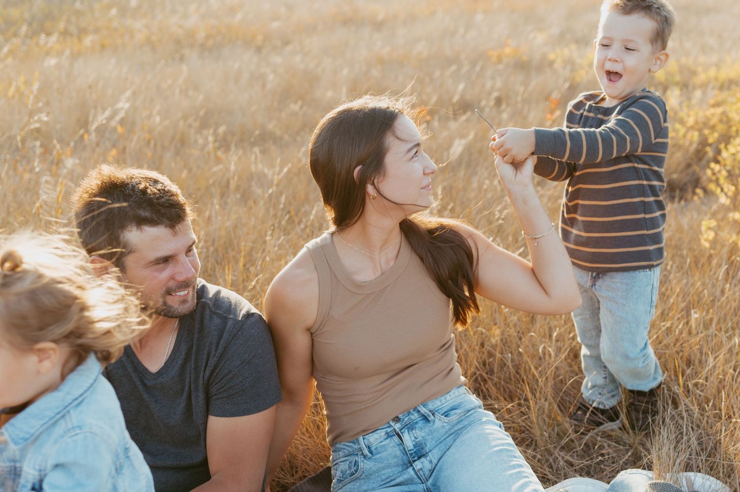 Family sharing joyful moment together while sitting in tall grass field.