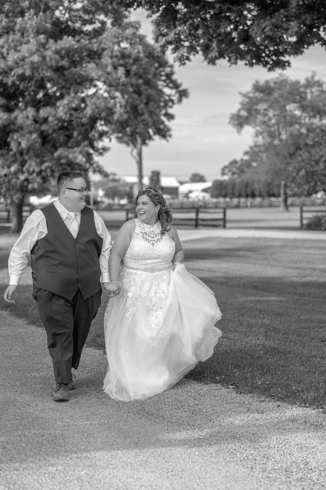 A couple walks together on a path during their wedding day, with trees and a manicured lawn in the background.