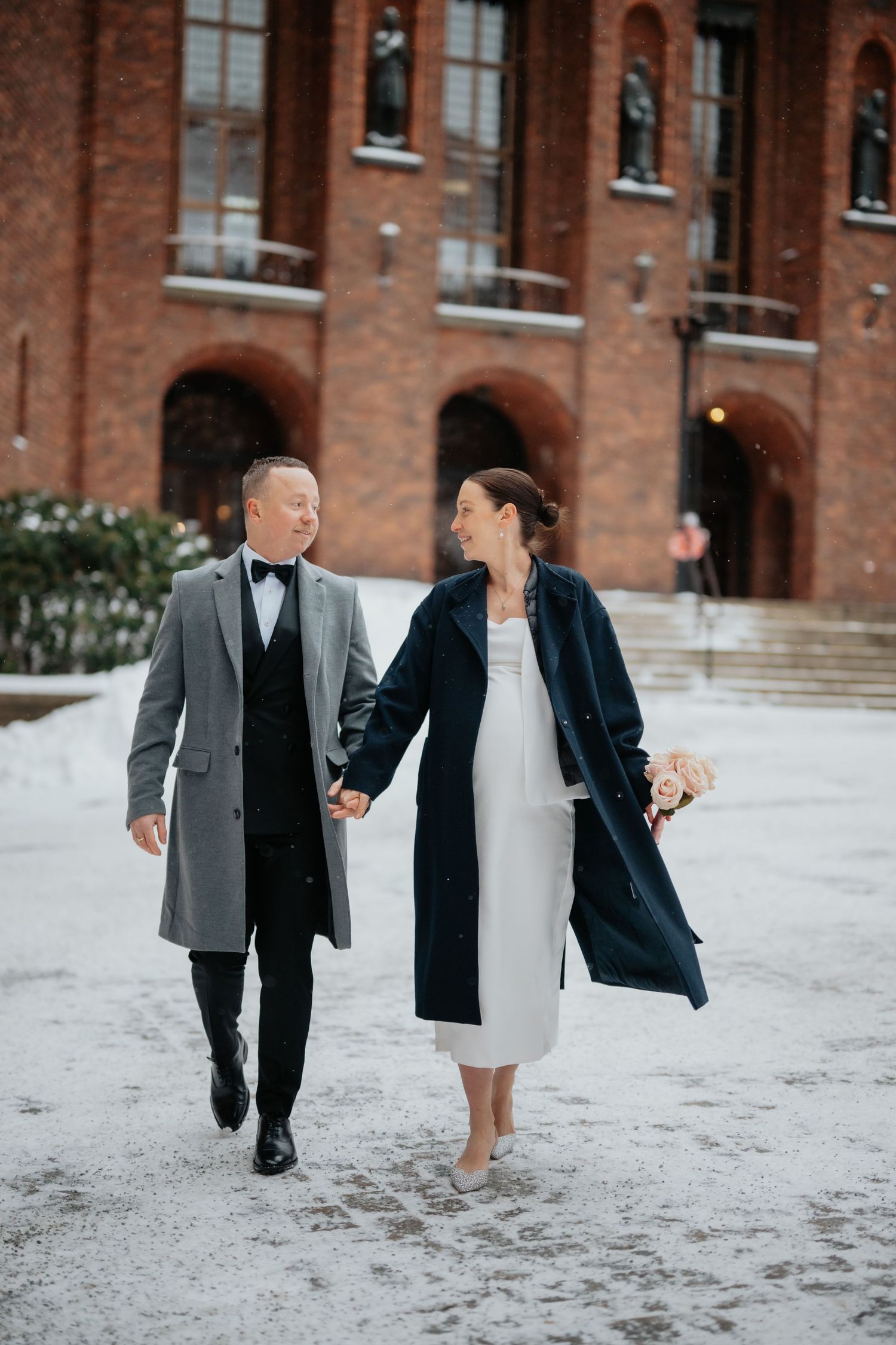 Brudparet poserar formellt framför en ståtlig vit herrgård på sin bröllopsdag.