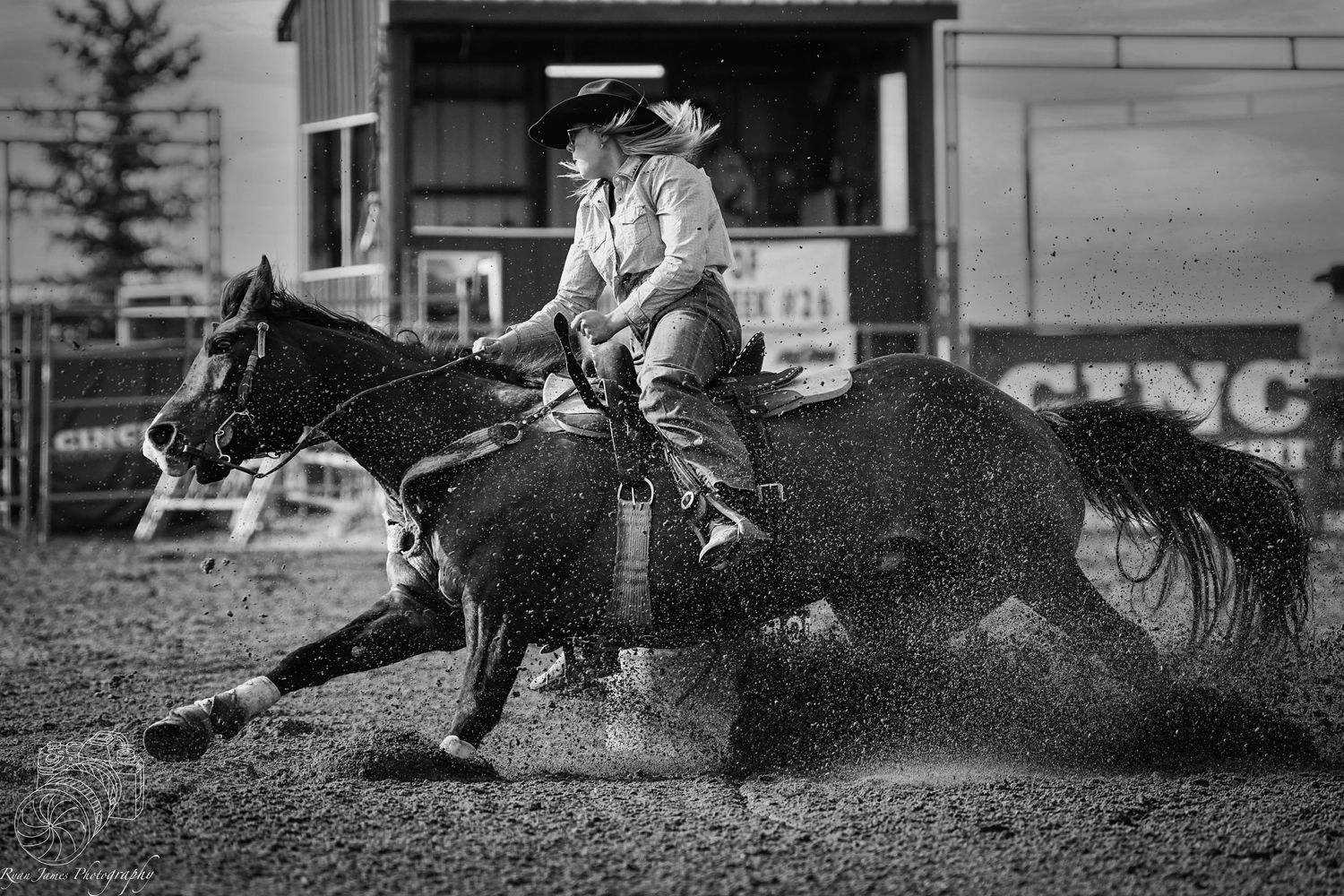 A dramatic black and white rodeo action shot shows a horse and rider kicking up dust during a barrel racing competition.