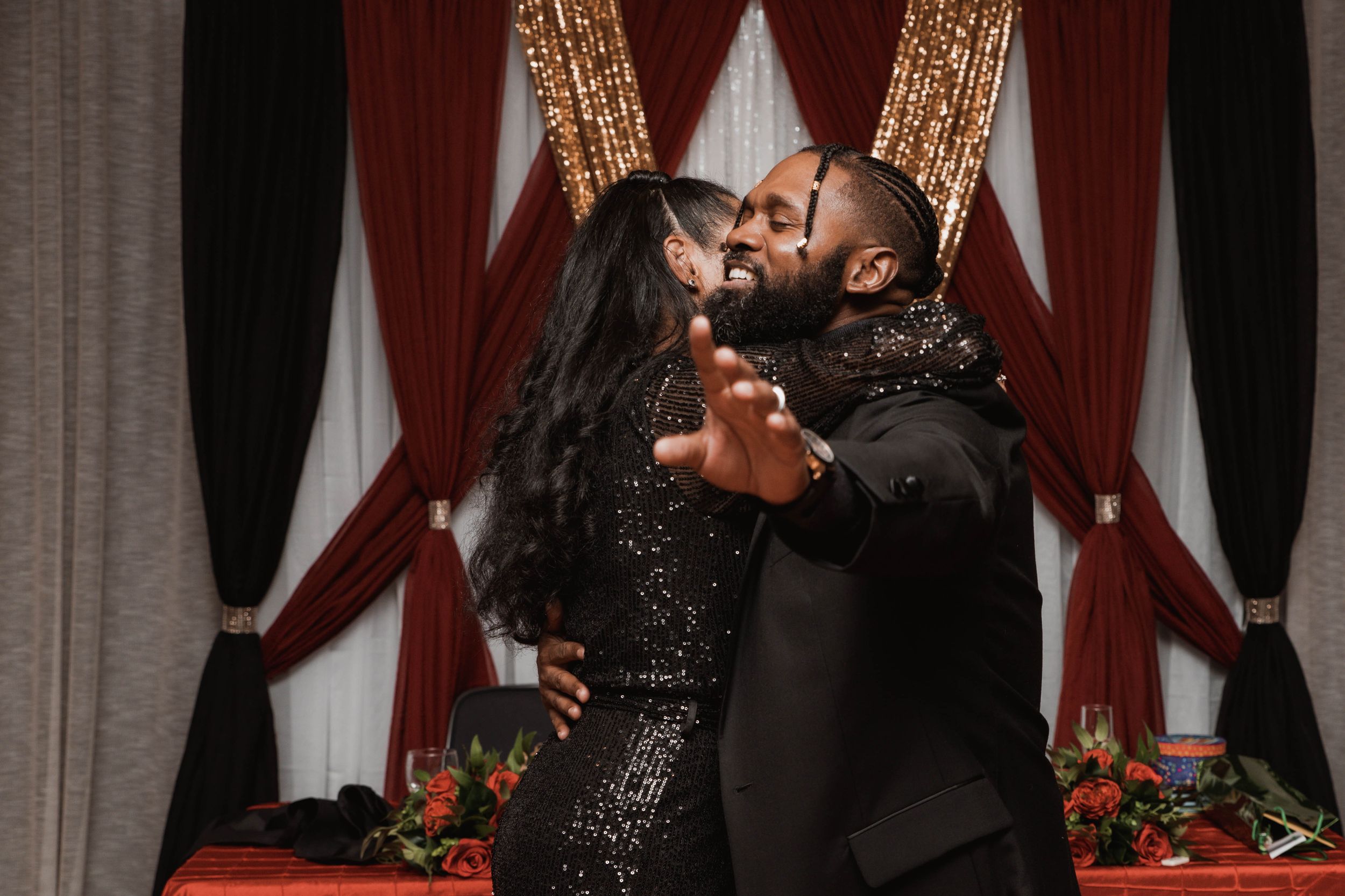 Couple dancing together in front of decorative red and gold curtains.
