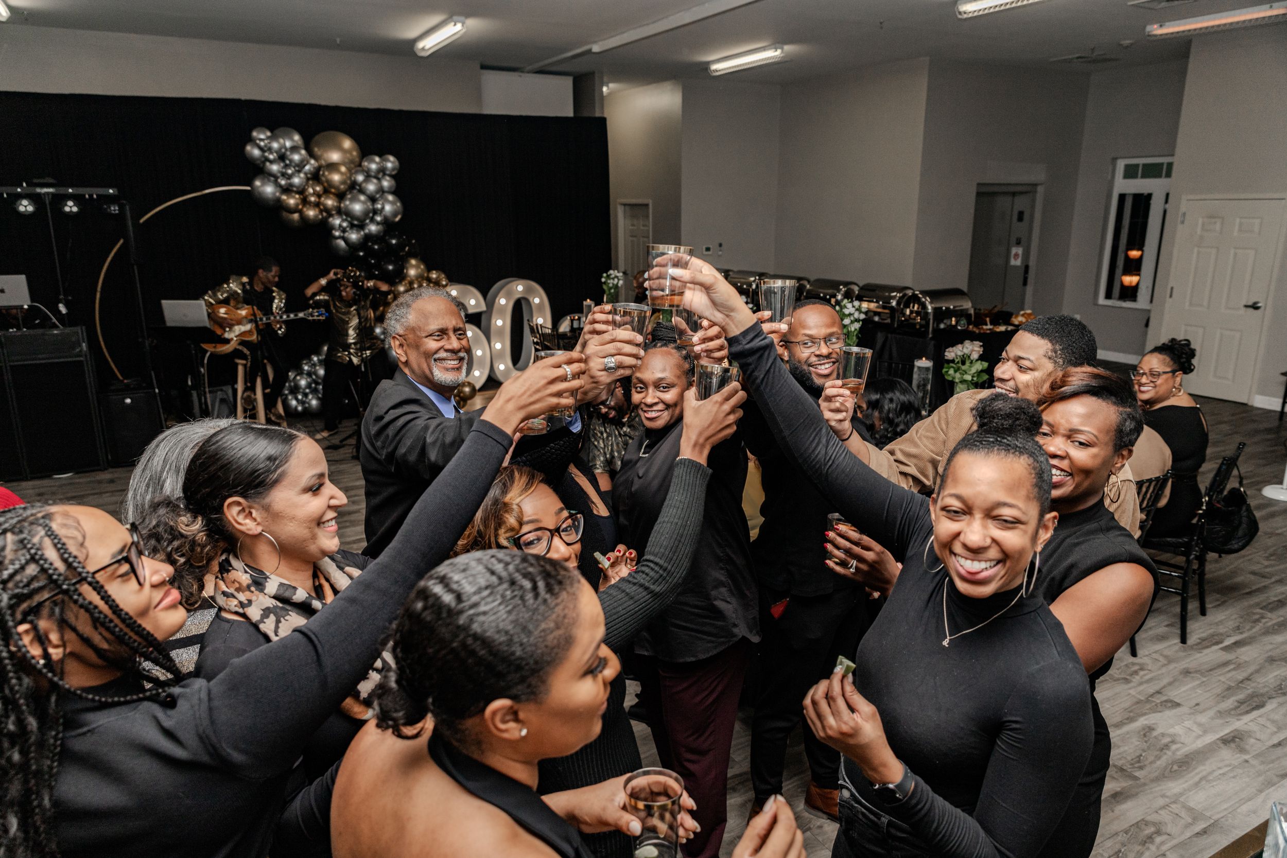 Large group raising glasses in celebratory toast during indoor event.