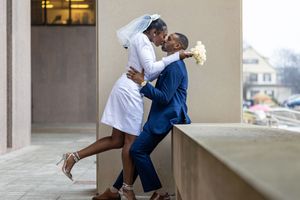Couple in wedding attire sharing romantic moment on outdoor ledge.