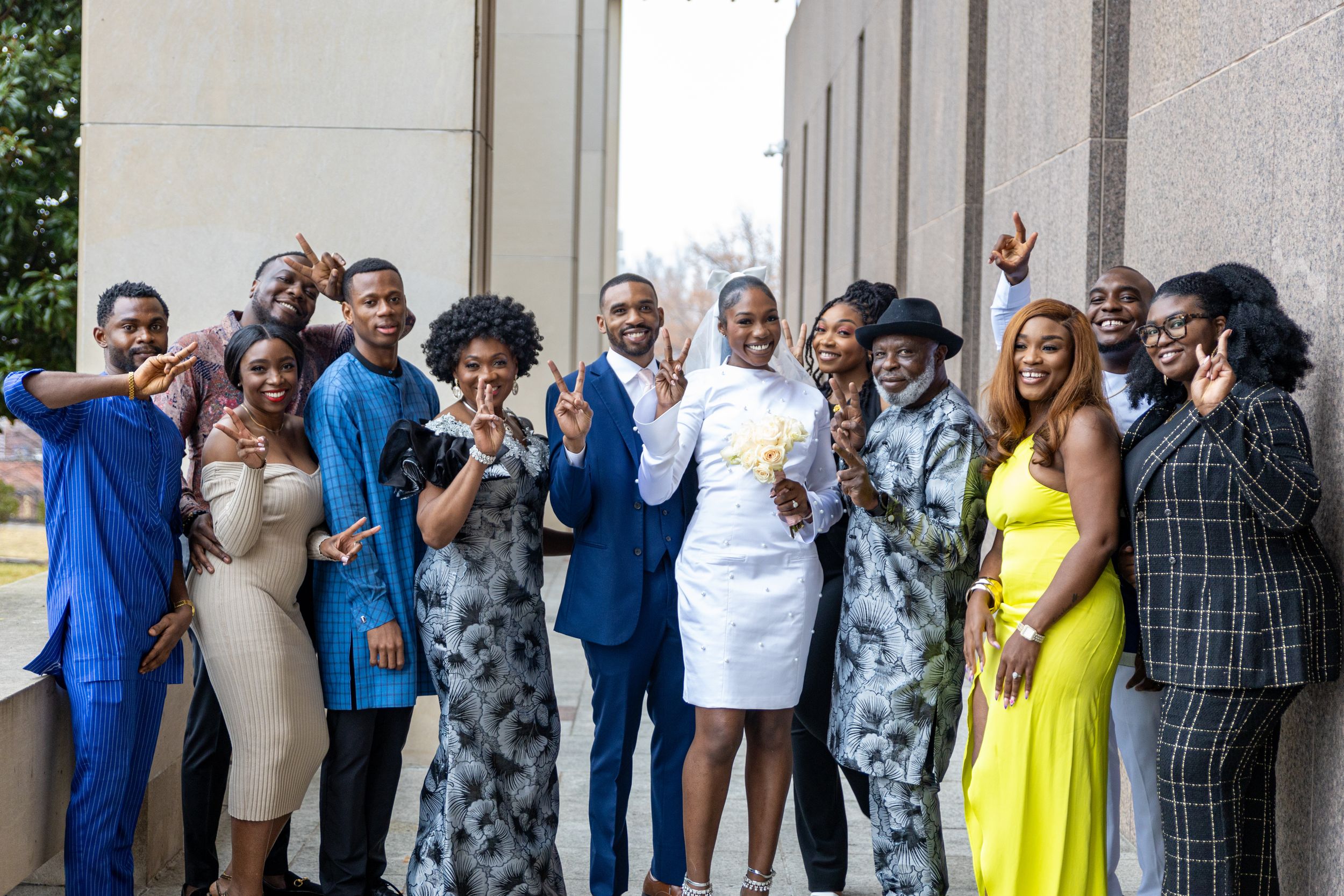 Wedding group photo with people in formal attire posing together outside.