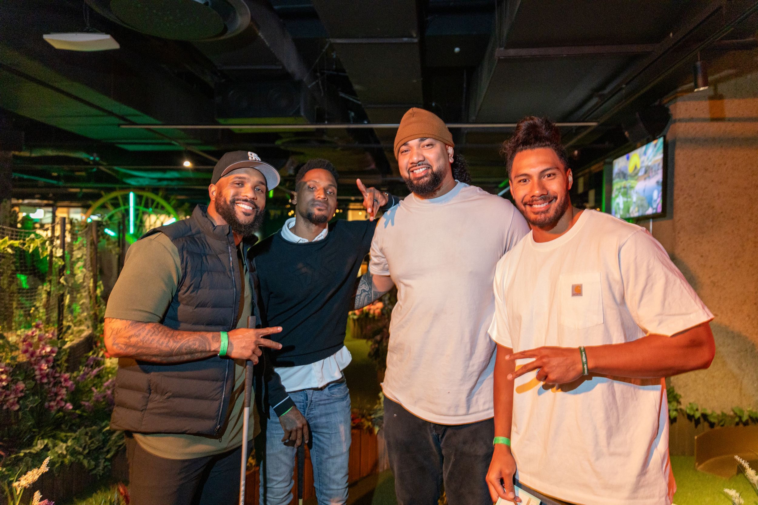 Four friends smiling and posing together in a trendy indoor venue with green decor.