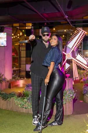Couple posing in front of neon windmill decoration at indoor entertainment venue.