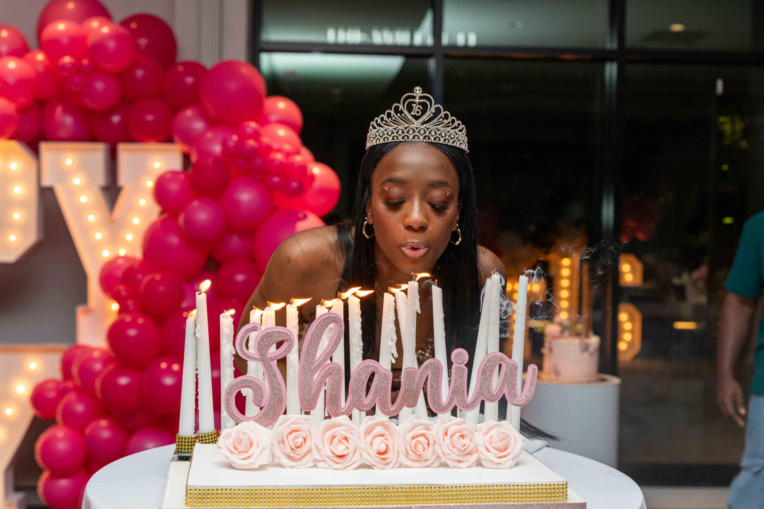 Birthday celebration with pink balloon arch and tiered cake decorated with roses.