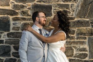 Wedding couple embracing against rustic stone wall during outdoor portrait session.
