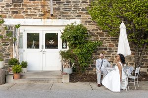 Newlyweds posing by white double doors of stone building with outdoor decor.