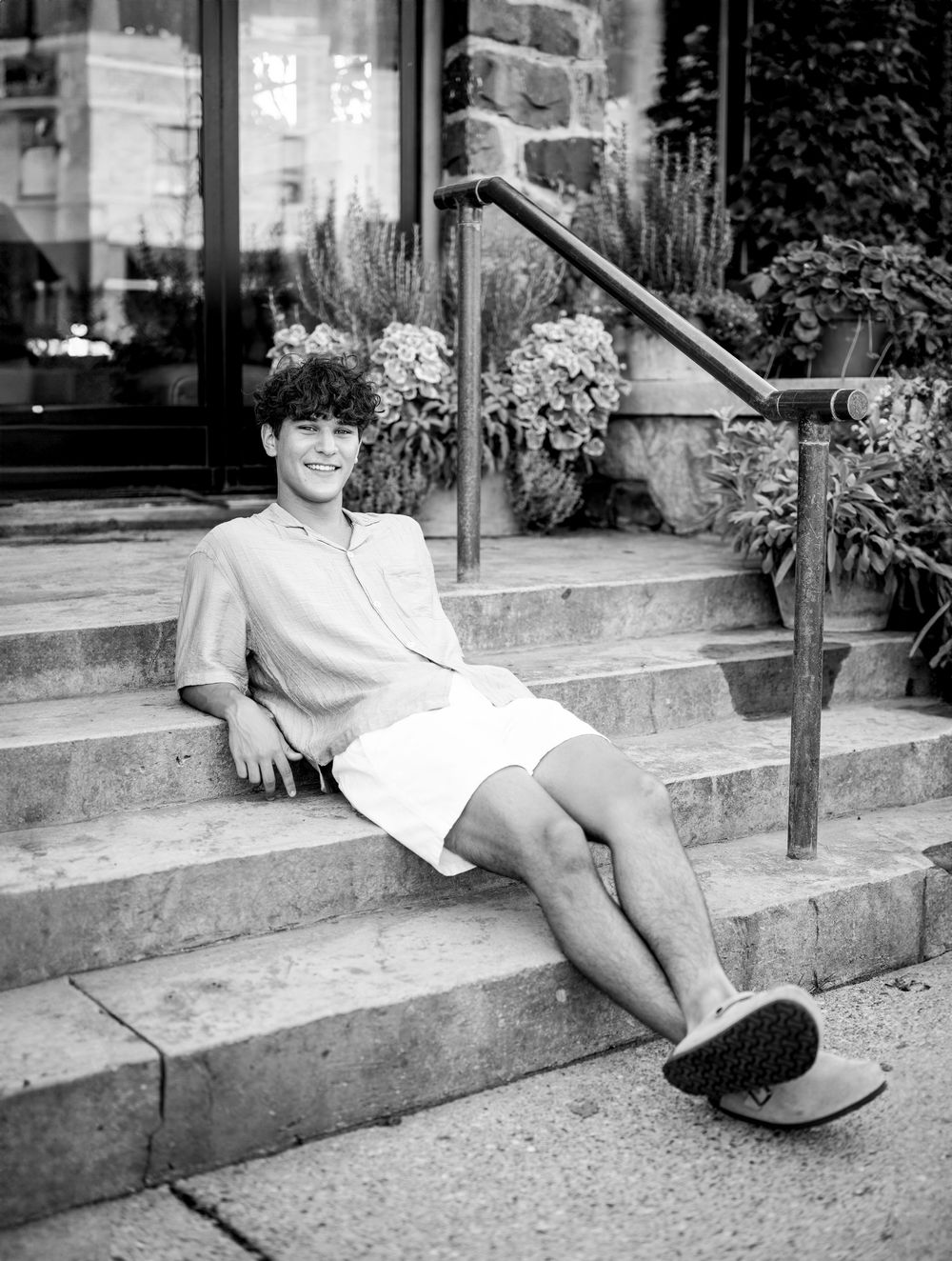 A black and white photo of someone relaxing on stone steps wearing casual summer attire.