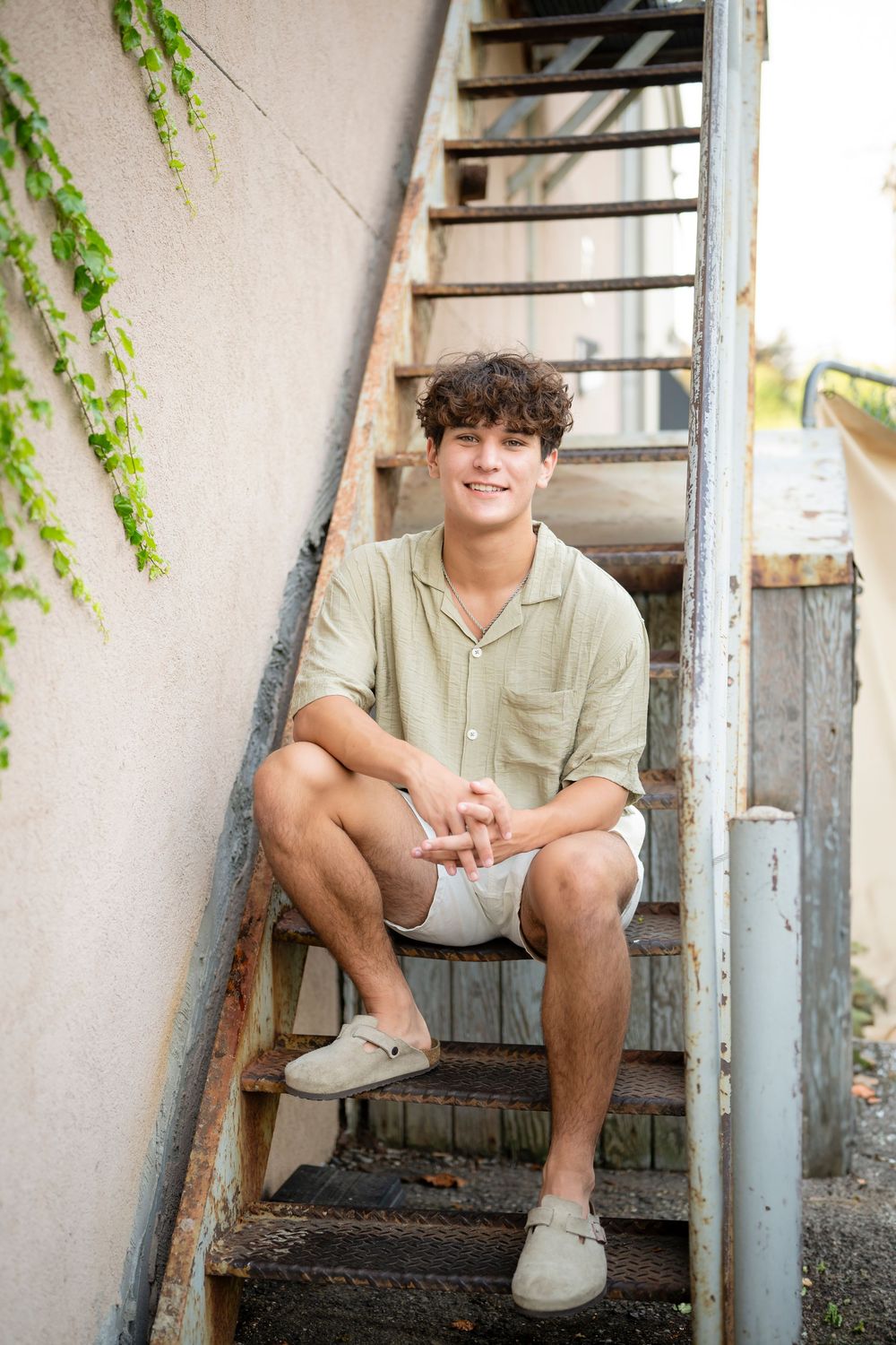 Someone sits casually on metal stairs wearing a light colored shirt and shorts.
