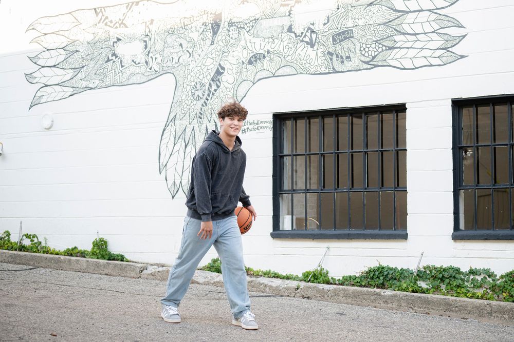Someone walking past a white wall with artistic murals wearing casual streetwear.