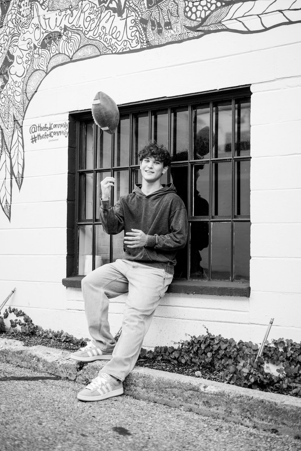 Black and white photo of someone tossing a football near a decorated wall.