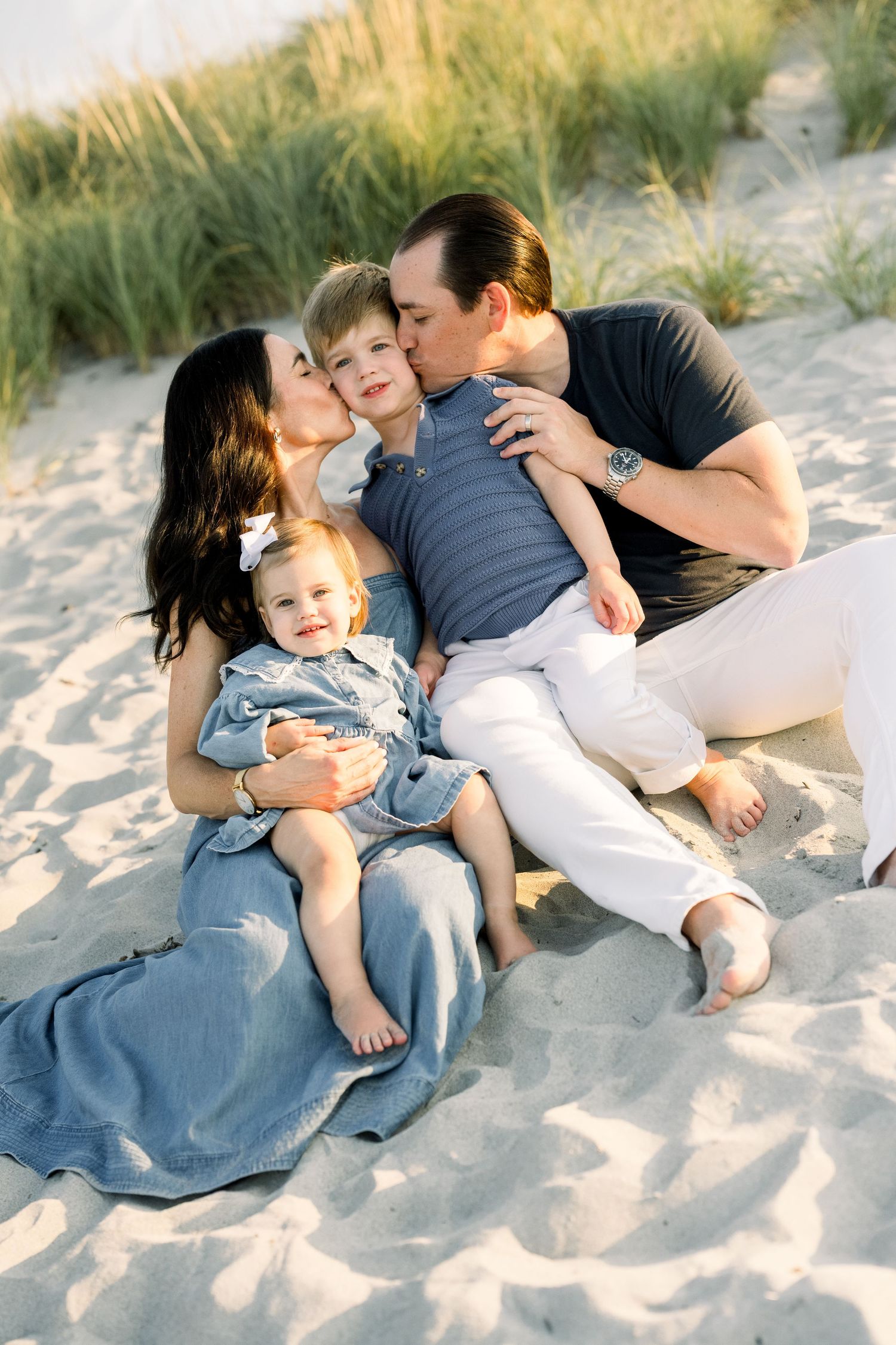A candid family moment captured on a sandy beach path with small children playing in the background.