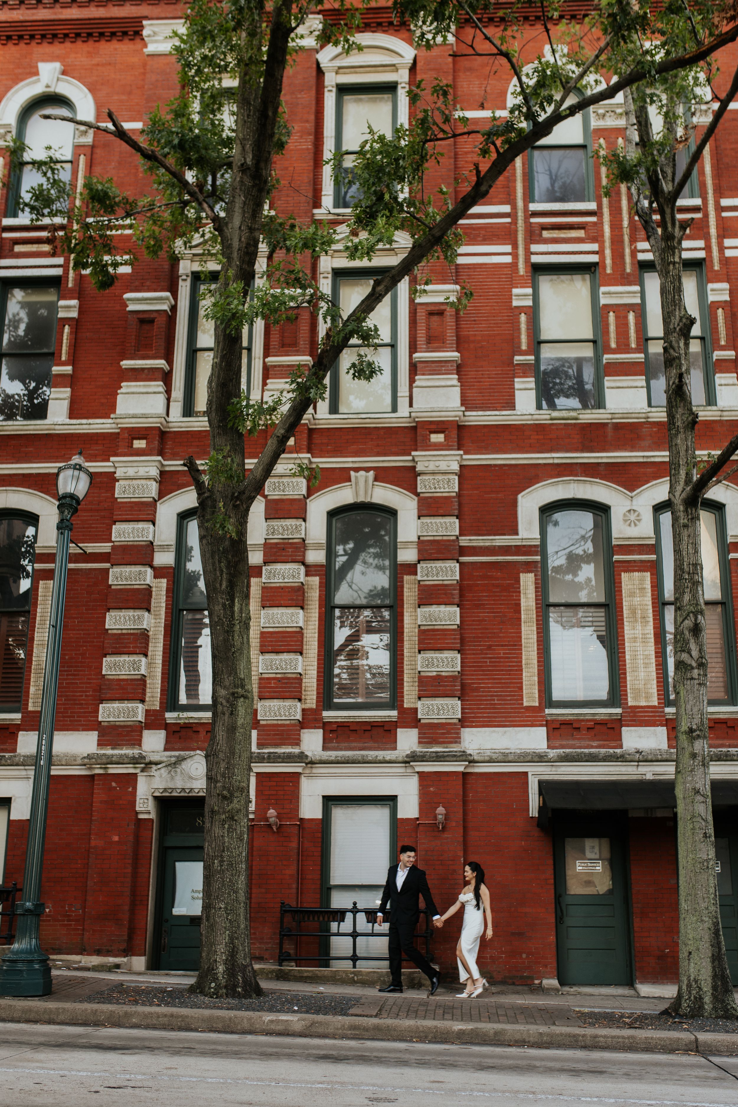 Red brick building facade with trees lining the sidewalk in an urban setting.