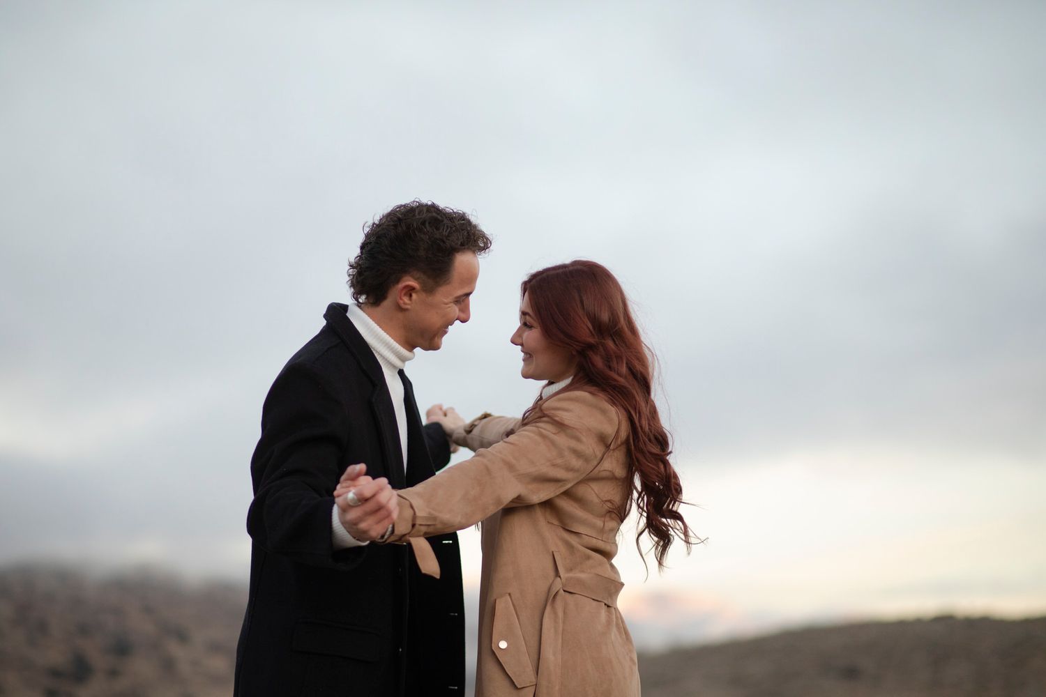 Couple is playfully holding hands with clouds and fog behind them.