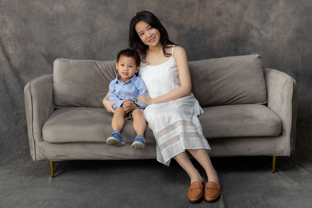A mother and child sit together on a modern grey sofa against a textured background.