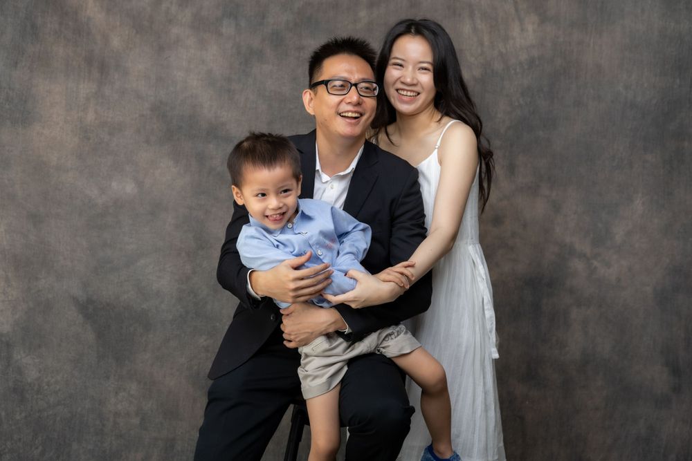 A loving family portrait with parents and child against a dark studio backdrop.