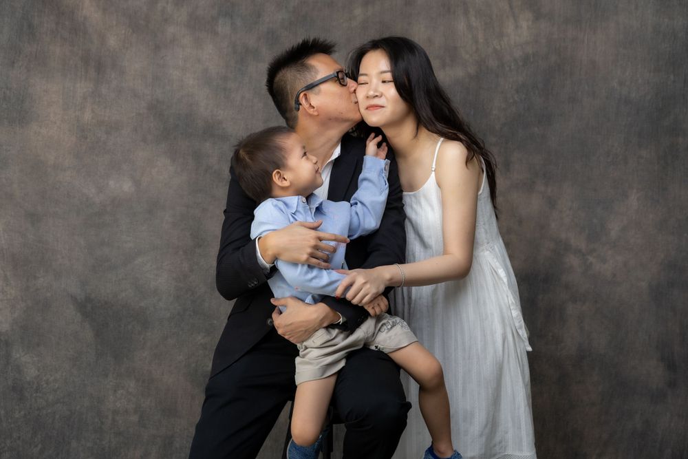 A tender family moment captured in a studio against a textured gray background.