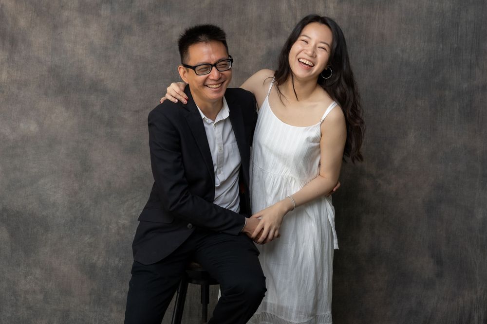 A couple in formal attire share a joyful moment against a dark studio background.