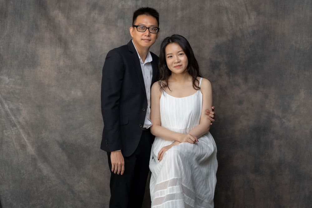 A couple in contrasting black and white outfits pose against a textured backdrop.