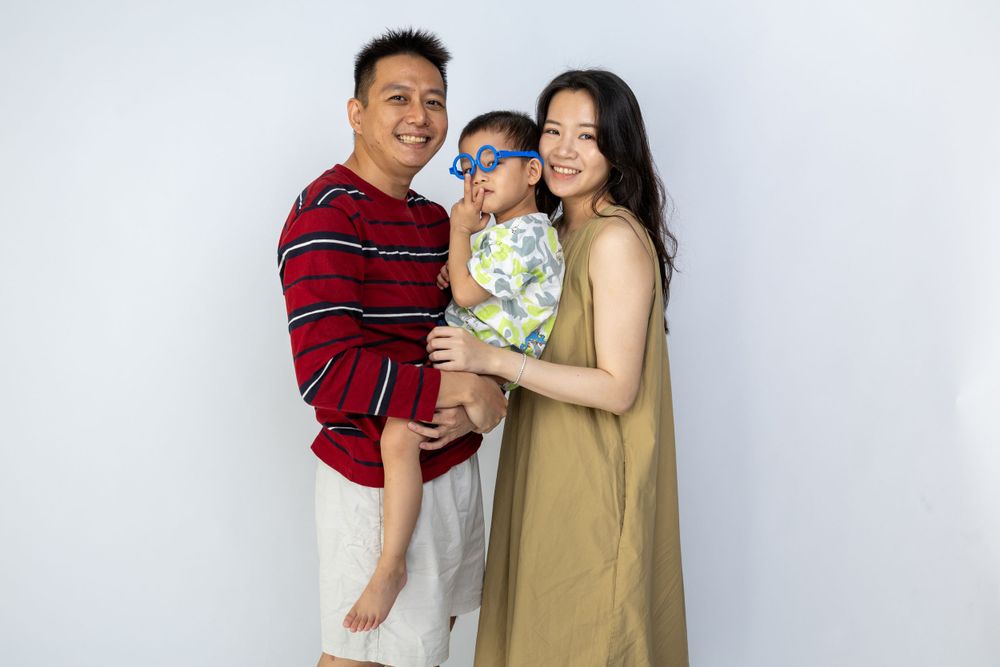 A family in casual attire poses together against a white background in a playful studio portrait.
