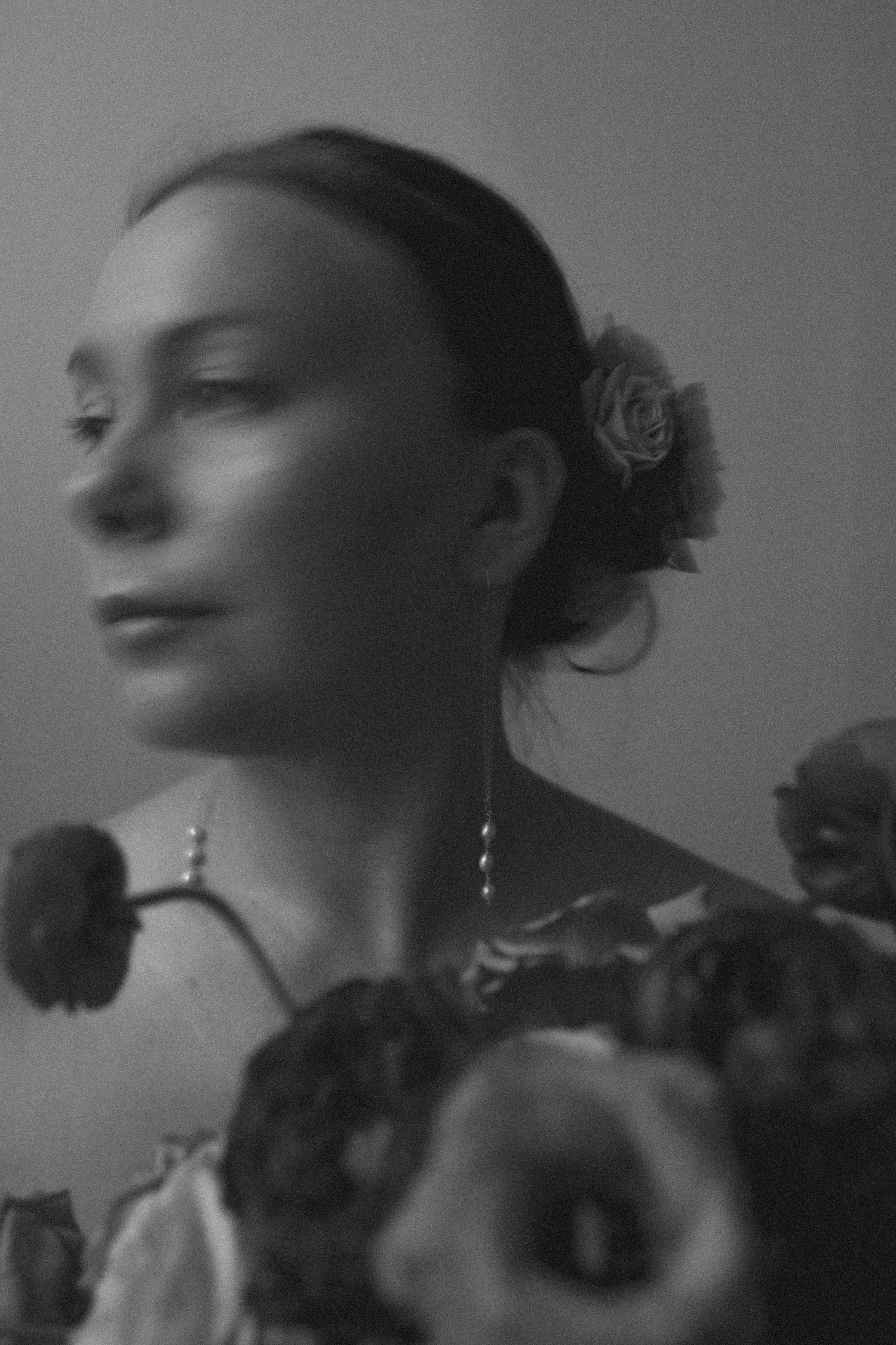 A dreamy black and white portrait showing an updo hairstyle with roses and dramatic side lighting.