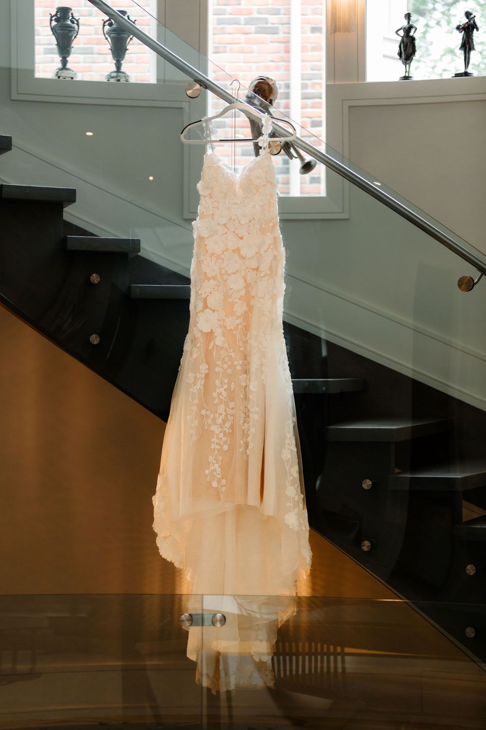 A delicate lace wedding dress hangs elegantly on a staircase with decorative urns in the background.