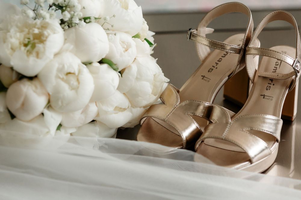 Champagne colored wedding heels displayed next to a lush white peony bouquet.