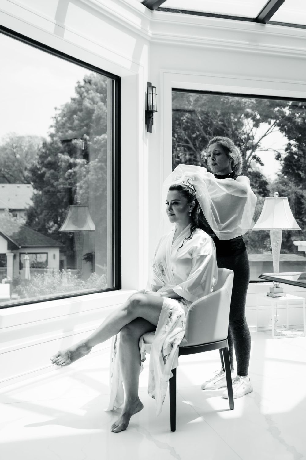 Black and white photo of hair styling session in modern room with large windows.