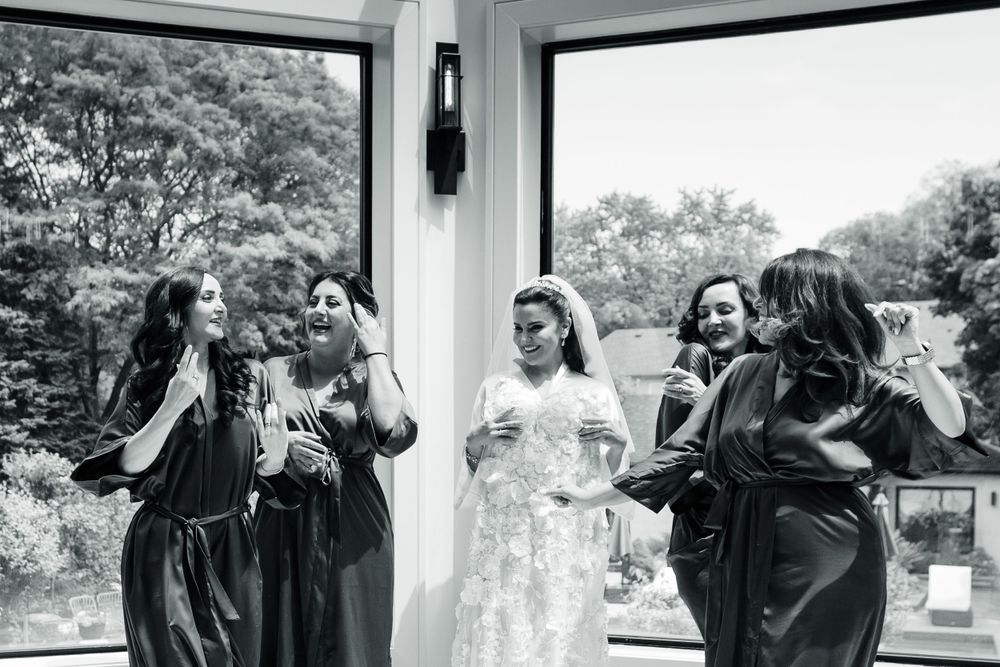 A black and white photo showing a wedding party laughing together while displaying the wedding gown.