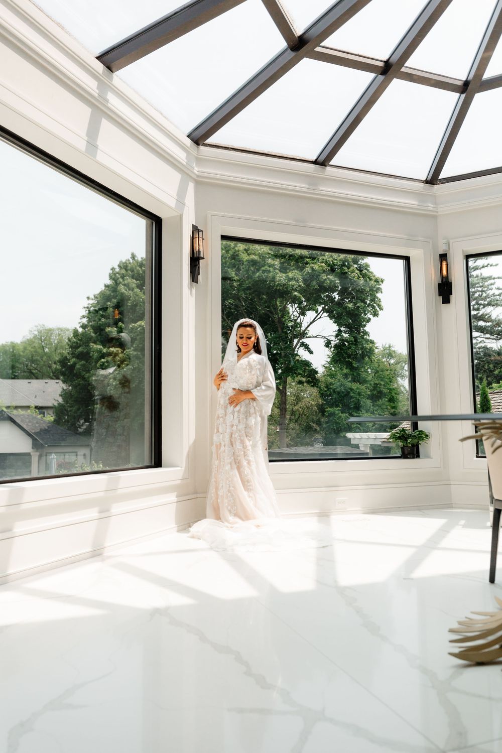 A sunlit bridal portrait in an elegant white conservatory with floor-to-ceiling windows.