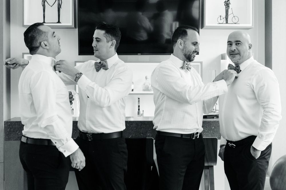 Groomsmen in white shirts and black bow ties sharing a casual moment together.