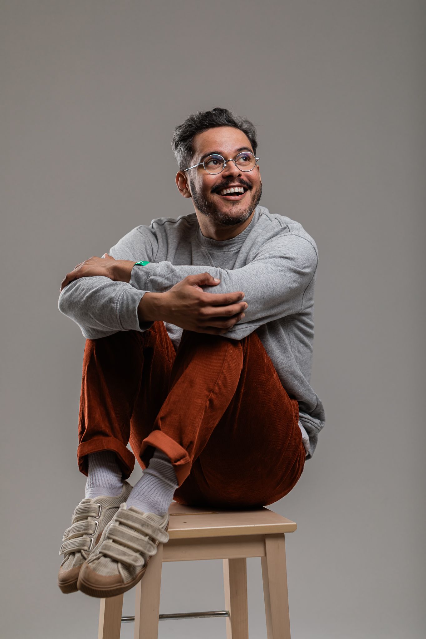Portrait of person in casual attire sitting on wooden stool against grey background.