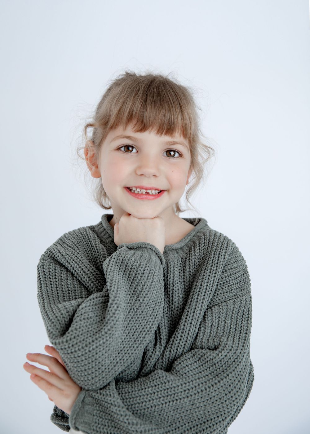 Portrait with joyful expression wearing cozy gray knit sweater against white background.